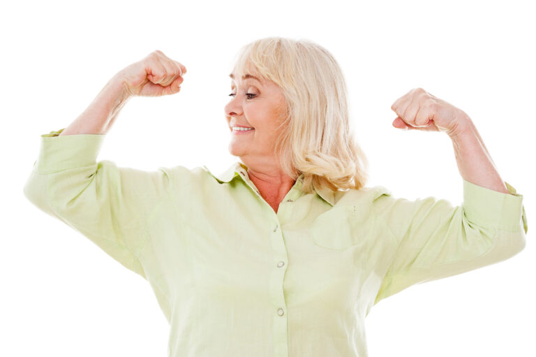 Feeling young and healthy. Cheerful senior woman checking her biceps and smiling while standing isolated on white background